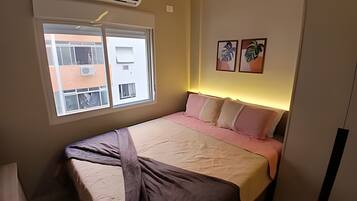 Een slaapkamer met een bed, een raam en twee kunstwerken aan de muur.