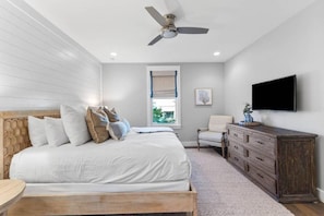 Quarto com cama, cômoda, cadeira, televisão e ventilador de teto.