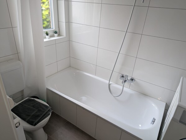 A bathroom with a white bathtub, a toilet, and a window with a view of greenery.