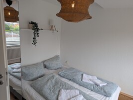 Quarto com cama, almofadas, planta pendente e luminária pendurada.