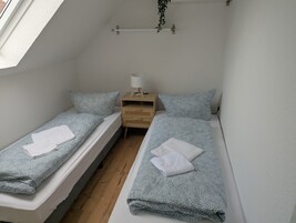 Eine kleine, einfache Unterkunft mit zwei Einzelbetten, einem Nachttisch mit Lampe und einer hängenden Pflanze.
