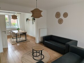 A modern living room with a black leather sofa, a round wooden coffee table, and a dining area with a table and chairs.