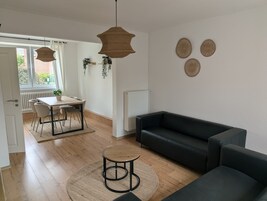 Uma sala de estar moderna com um sofá de couro preto, uma mesa de centro redonda de madeira e um espaço de jantar com mesa e cadeiras.