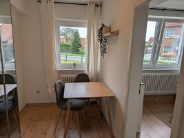 Ein Zimmer mit Holzboden, einem Tisch mit zwei Stühlen, einem Fenster mit Vorhängen und einer Heizung.