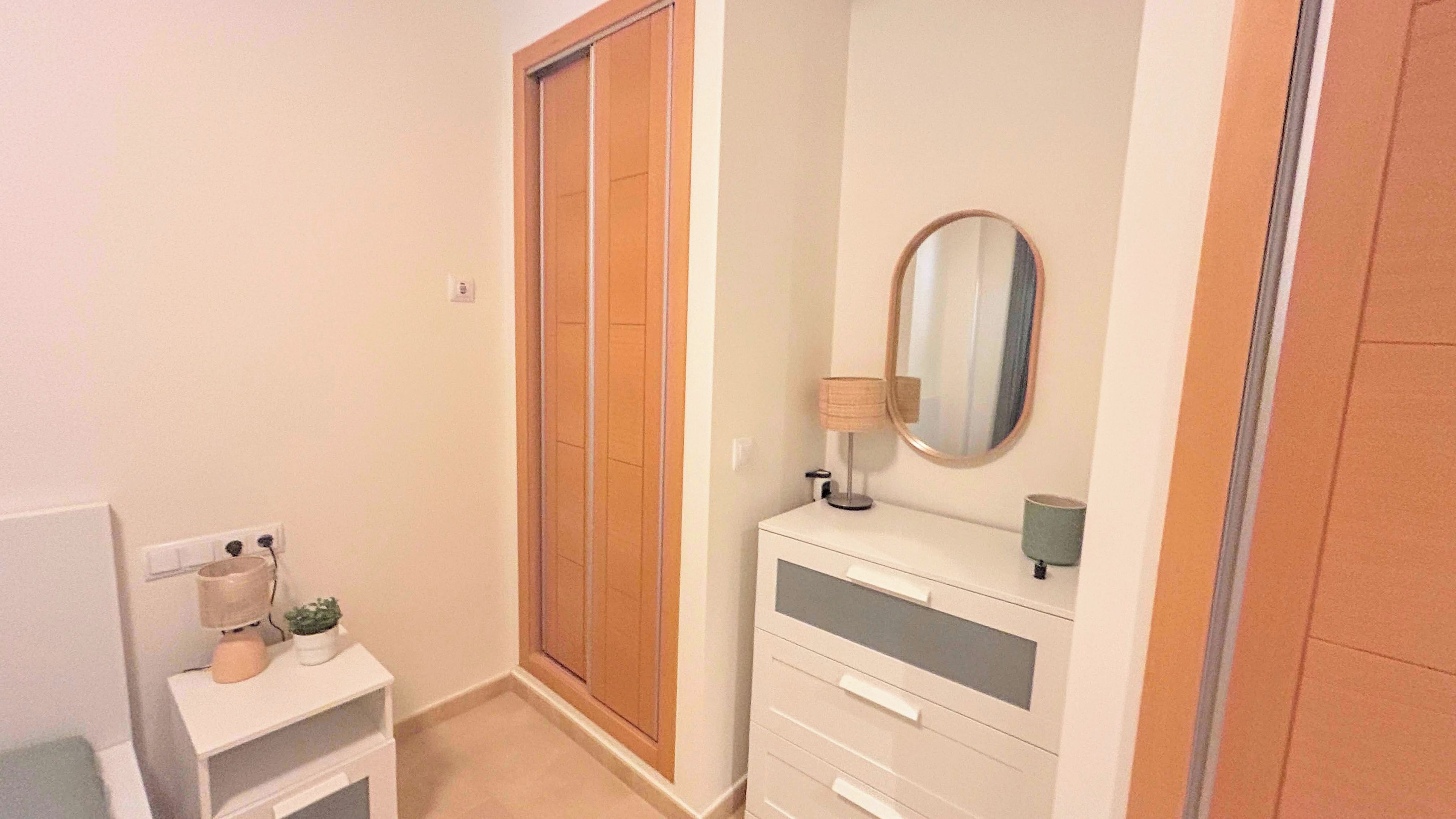 Une chambre à coucher avec une armoire, une table de chevet avec une lampe et un miroir.