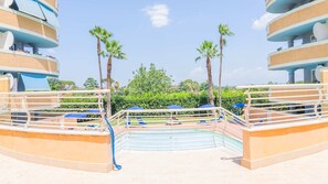 A resort pool area with a circular design, palm trees, and a clear sky. - Grazioso Bilocale con Piscina e Terrazza Wi-fi AC (Rome)