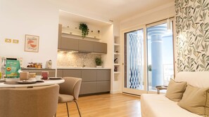 A modern kitchen with a built-in oven, a dining area with a round table and chairs, and a sliding glass door leading to a balcony. - Grazioso Bilocale con Piscina e Terrazza Wi-fi AC (Rome)