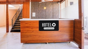 A hotel reception desk with a wooden finish, a ceiling fan above, and a staircase to the left. - Hotel O Palava Dombivali (Mumbai)