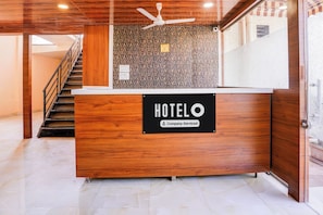Taulell de recepció d'hotel amb acabat de fusta, un ventilador al sostre i una escala a l'esquerra.
