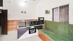 Een hotel receptie met een receptiebalie, een bank en een bord aan de muur met de naam van het hotel.