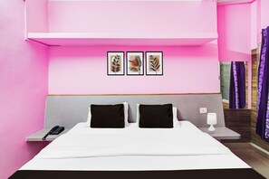 Ein Hotelzimmer mit einem Bett, zwei Nachttischen, einem Telefon, einer Lampe und drei gerahmten Kunstwerken an der Wand.