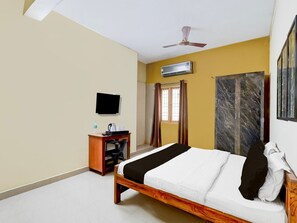 A hotel room with a bed, a television, a desk with a chair, an air conditioning unit, and a wardrobe.