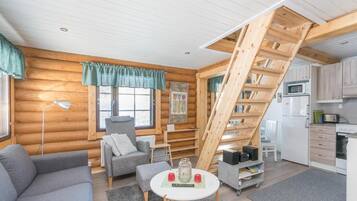 A log cabin interior with a staircase, a sofa, a dining table, and a kitchenette.