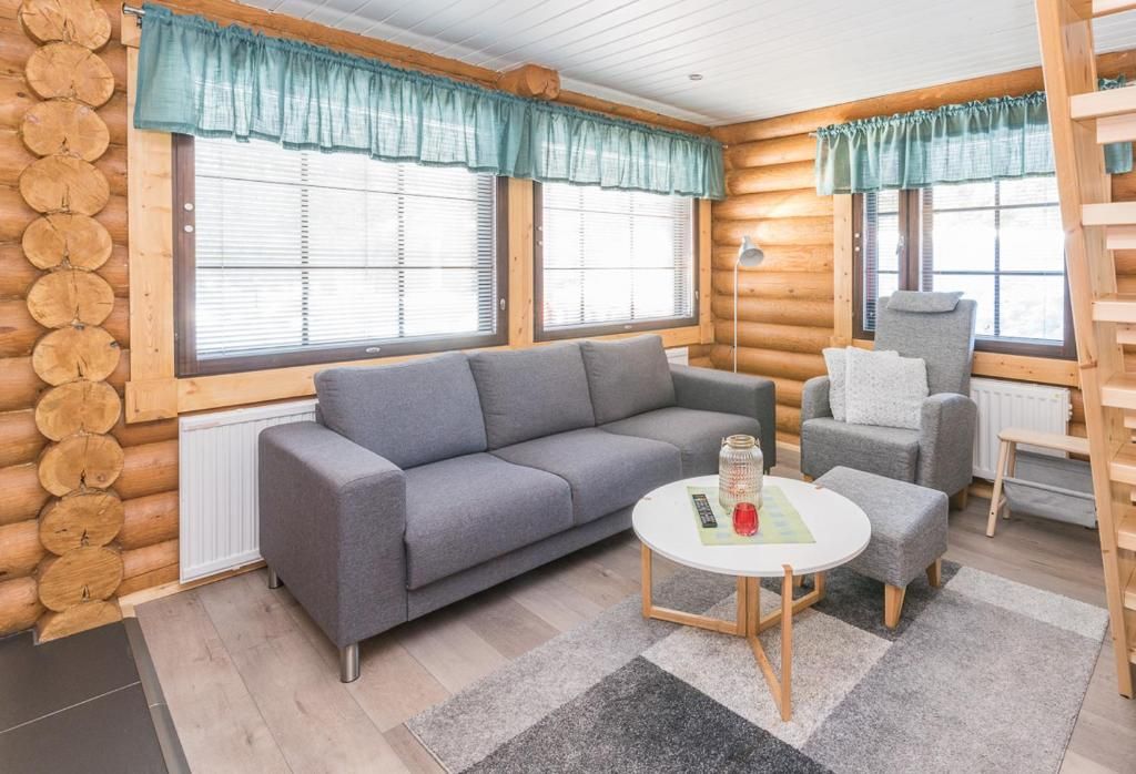 Ein rustikales Blockhaus-Interieur mit einem grauen Sofa, einem kleinen runden Tisch und einem grauen Sessel.