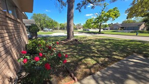 A residential street with a brick house, a tree, and a flower bed with red flowers. - Spacious 3BR Home for a Houston Getaway (Houston)
