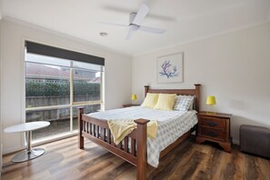 Ein Schlafzimmer mit Bett, Nachttischen, Deckenventilator, Fenster und Blick nach draußen.