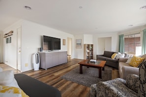 A modern living room with a flat-screen TV, grey sofa, and a coffee table. - Bimble Street Beach House - 300 Meters to beach & Pet Friendly (Melbourne)