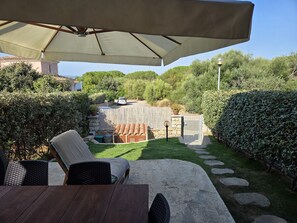 Eine Terrasse mit Tisch und Stühlen, ein überdachter Sitzbereich und Blick auf den umliegenden Garten und die Hügel.