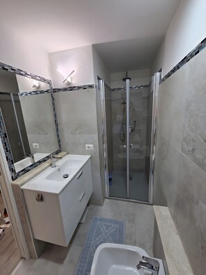 Ein modernes Badezimmer mit einer gläsernen Duschkabine, einem weißen Waschbecken und einem großen Spiegel mit Mosaikbordüre.