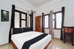 Una habitación de hotel con cama, una silla, escritorio y ventana con cortinas.