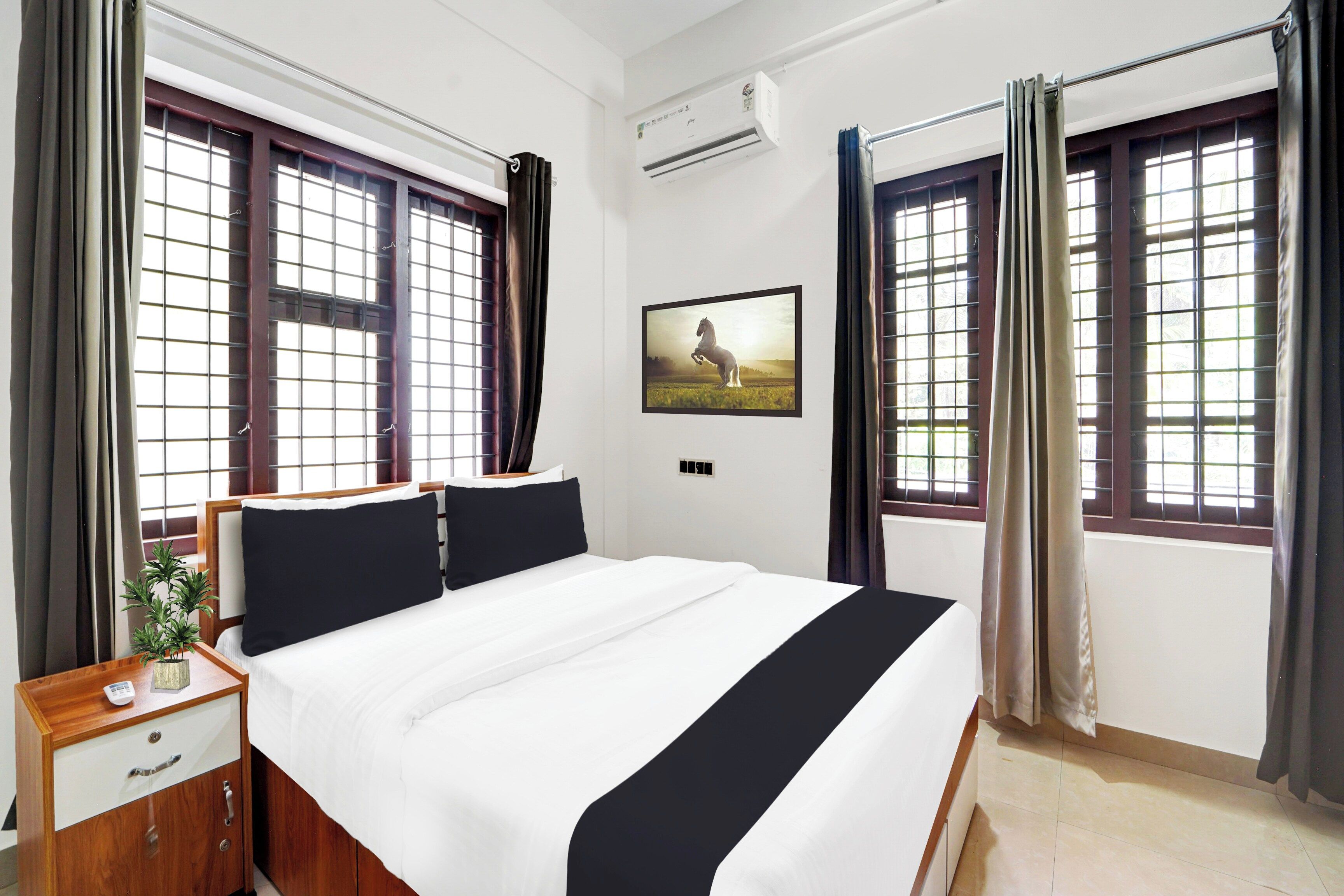 Habitación de hotel con cama, mesita de noche, planta y un cuadro en la pared.