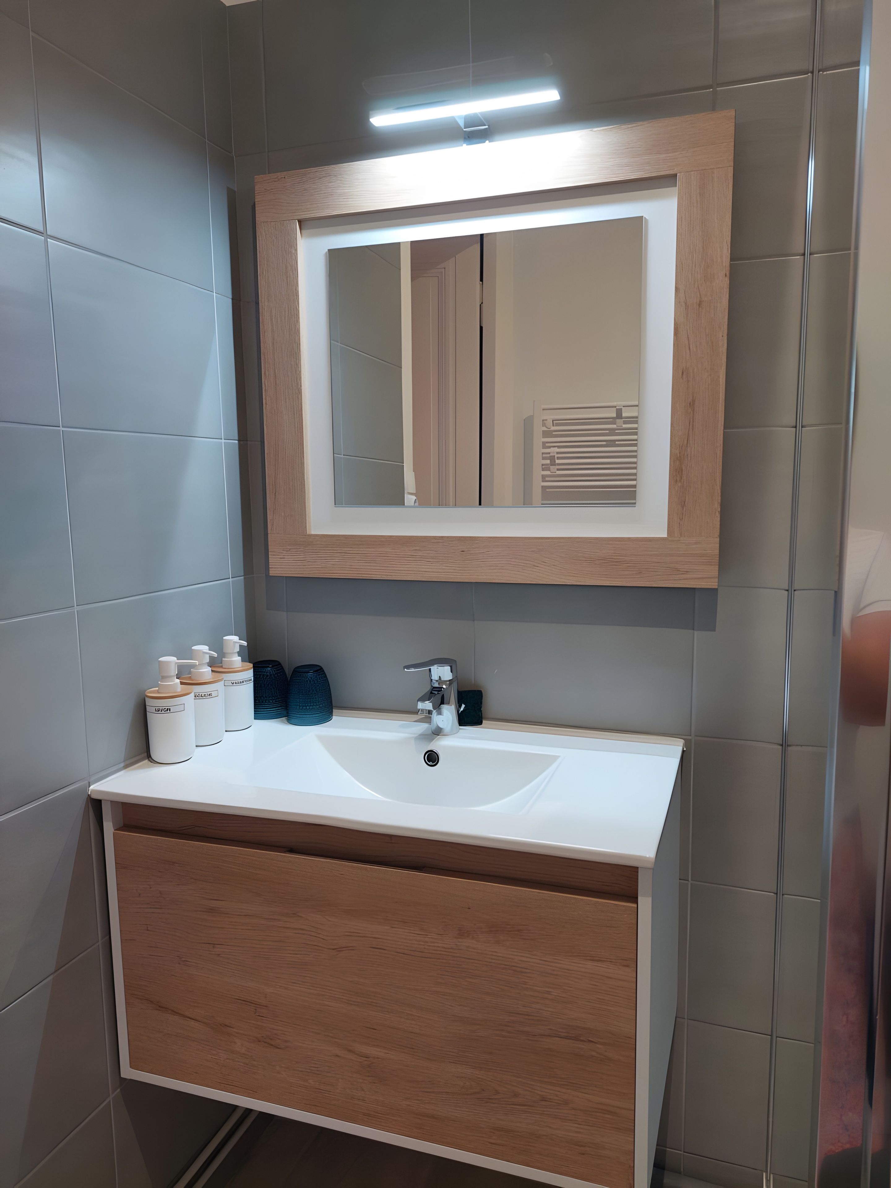 Une salle de bain avec un lavabo blanc, un meuble-lavabo en bois et un miroir avec un cadre en bois.
