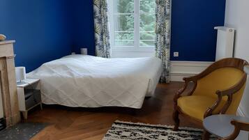 Une chambre à coucher avec un lit, une chaise, une table de chevet, une lampe et une fenêtre avec des rideaux.