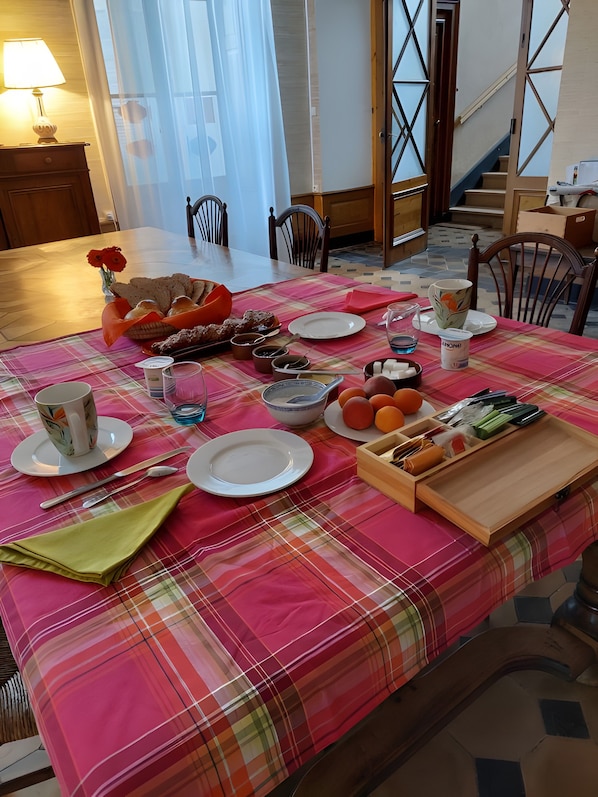 A dining table set with plates, cutlery, and a variety of food items, including bread and fruits, in a room with a staircase and chairs.