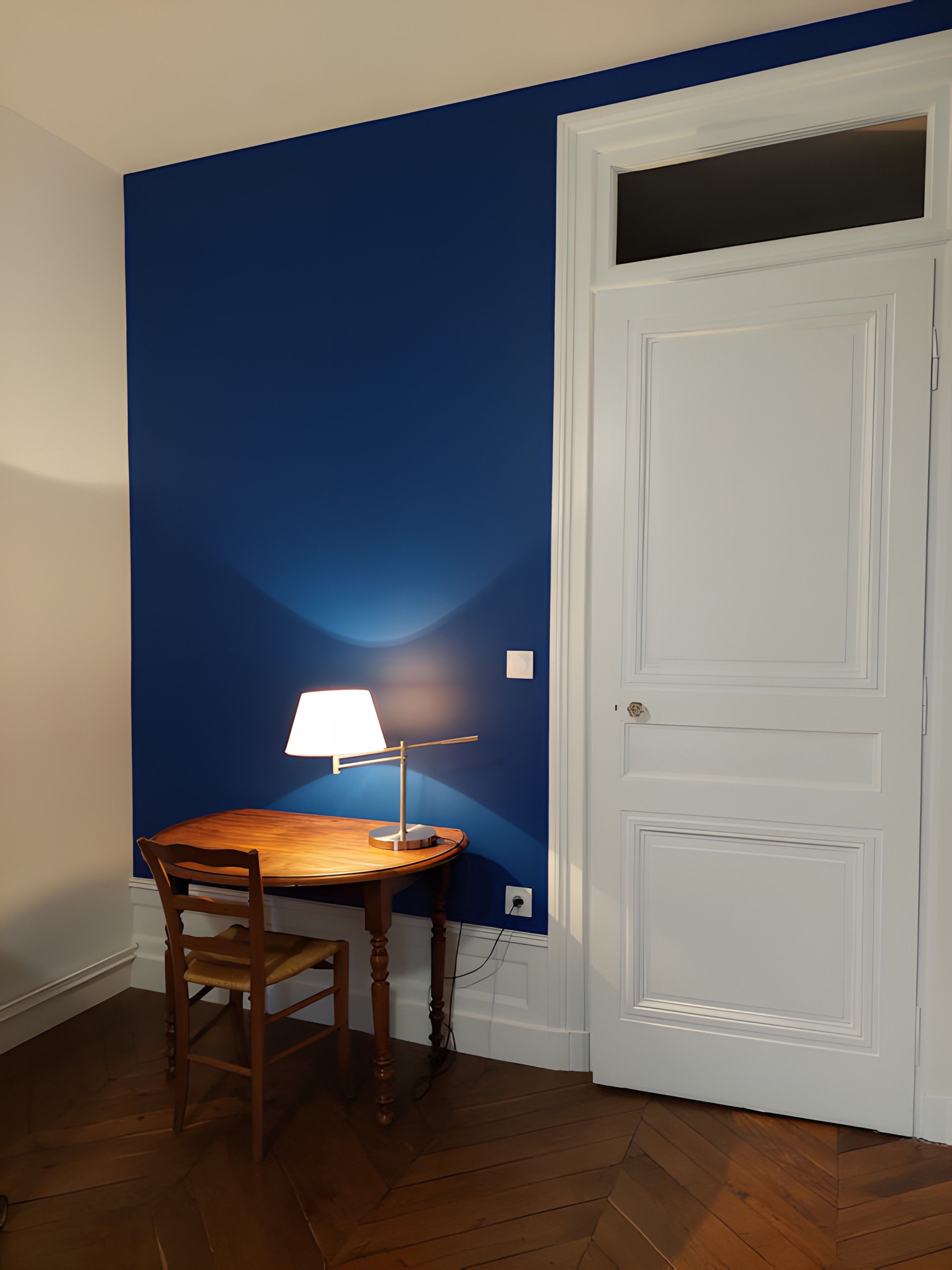 Une pièce avec une table et une chaise en bois, une porte blanche et des murs bleus.