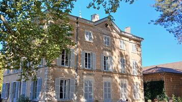 Un bâtiment à deux étages doté d’une façade symétrique, de nombreuses fenêtres avec volets et d’une cour pavée aménagée avec des sièges extérieurs.