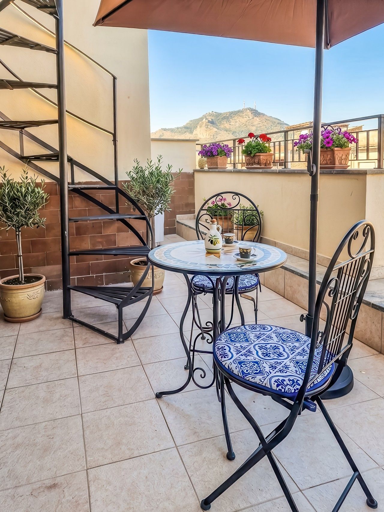 Eine Terrasse mit einem runden Tisch, zwei Stühlen, einem Blumentopf und einer Metalltreppe.