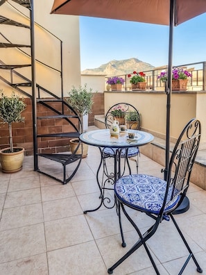 Eine Terrasse mit einem runden Tisch, zwei Stühlen, einem Blumentopf und einer Metalltreppe.