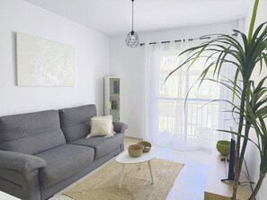 A modern living room with a grey sofa, a white coffee table, a large plant, and a painting on the wall. - Vibes Center Flat - El Mirador (Tarifa)