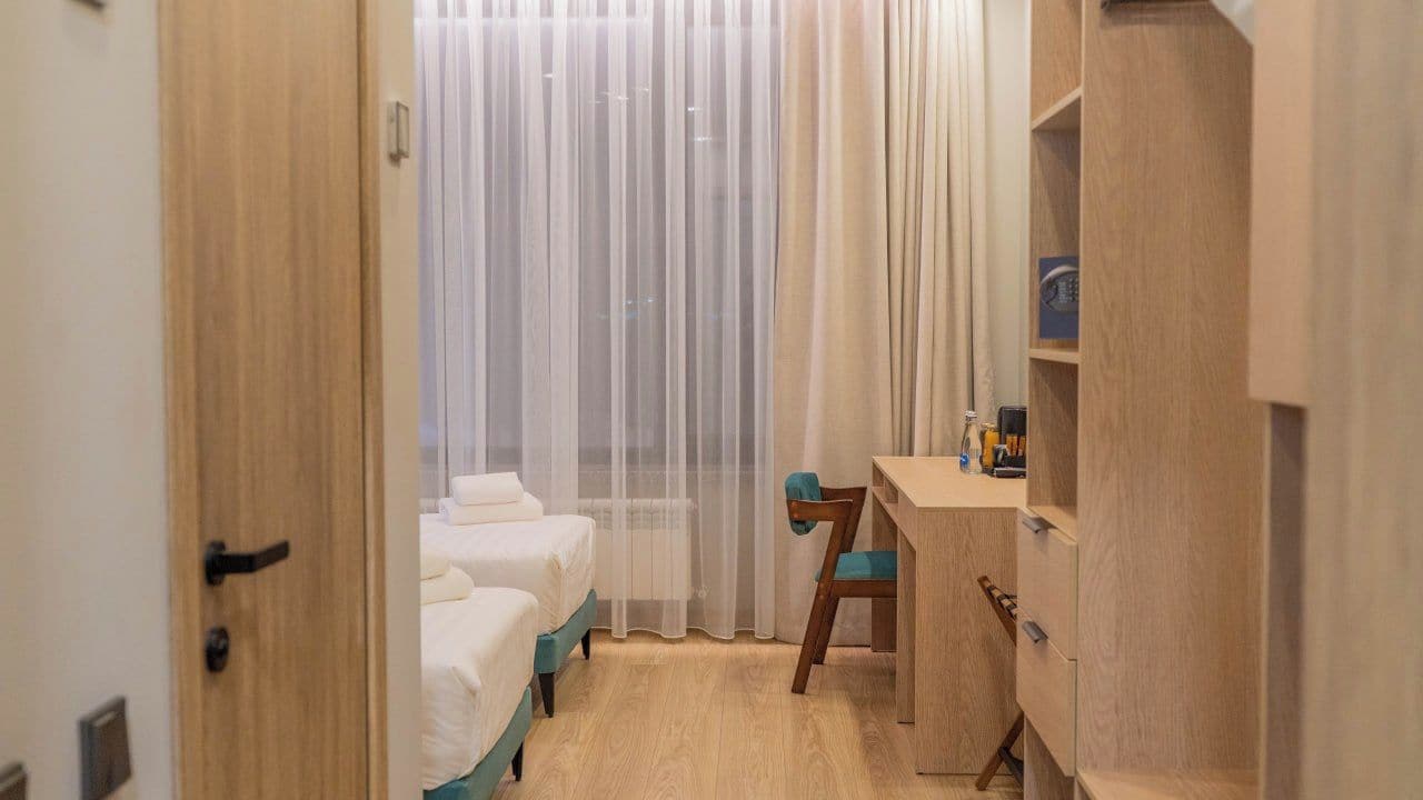 Ein Hotelzimmer mit einem Holzschrank, einem Schreibtisch mit Stuhl und zwei Betten.