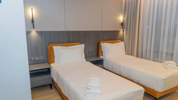 Habitación de hotel con dos camas individuales, una mesita de noche, una lámpara de pared y una ventana con cortinas.