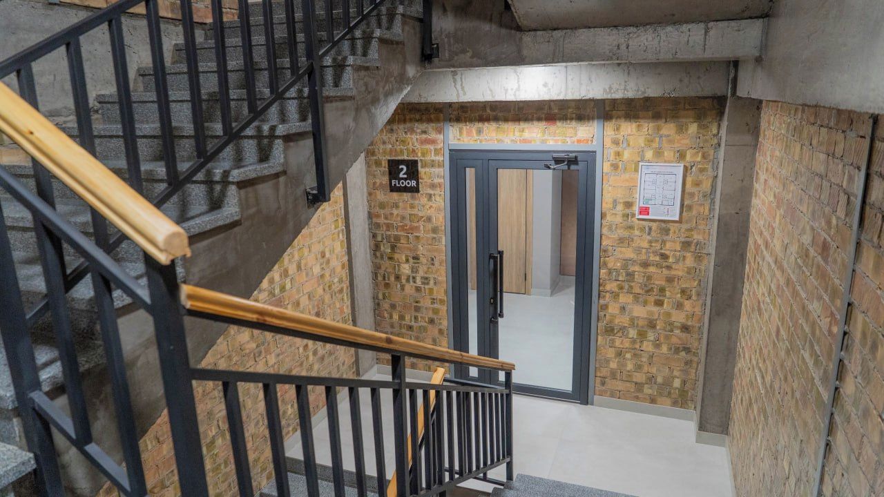 Una escalera que lleva al segundo piso, con un muro de ladrillo y una puerta.
