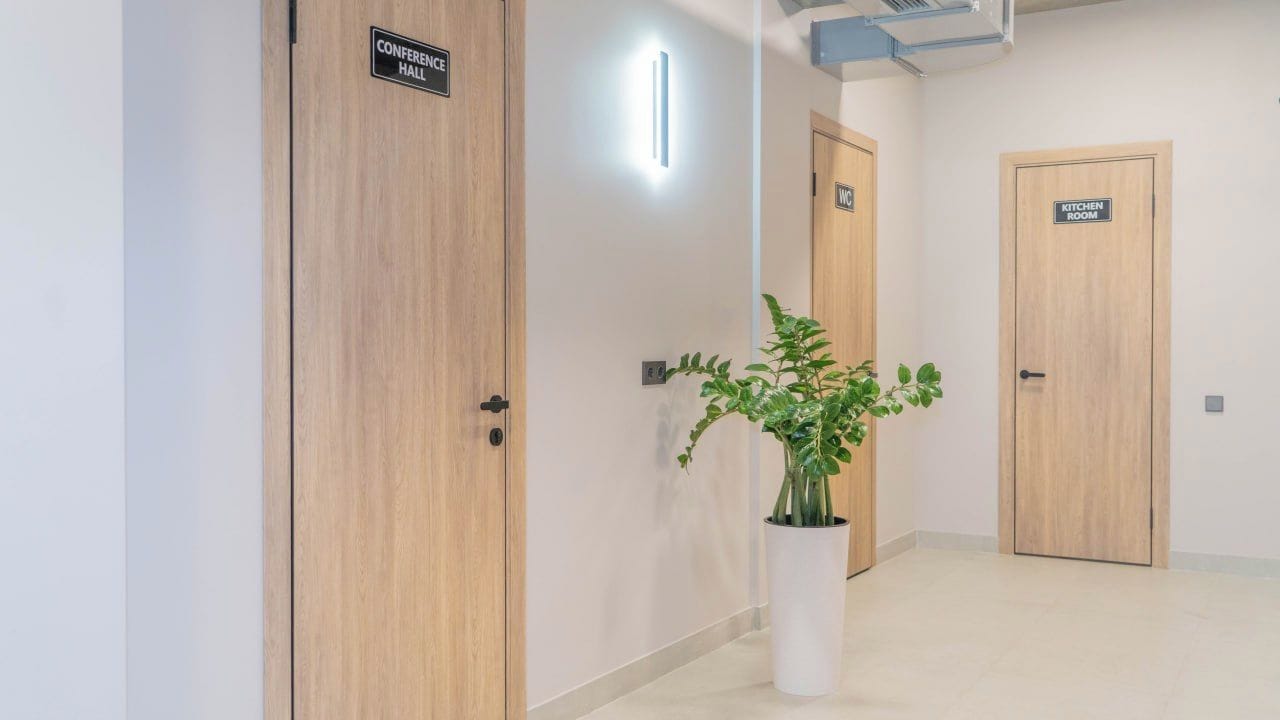 A hallway with wooden doors labeled 'Conference Hall' and 'Kitchen Room,' and a potted plant in the center.