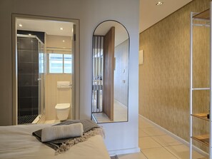 Une chambre d’hôtel moderne équipée d’un lit, d’une douche, de toilettes et d’un grand miroir.