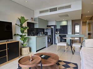 A modern living room with a TV, a coffee table, and a large plant. - Modern Apartment Secure and Spacious (Cape Town)