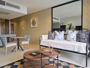 A modern living room with a sofa, two round coffee tables, a dining table with chairs, and a large mirror. - Modern Apartment Secure and Spacious (Cape Town)