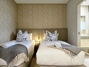 A hotel room with two beds, a headboard, bedside lamps, and a view of the bathroom. - Modern Apartment Secure and Spacious (Cape Town)