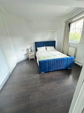 Un dormitorio con una cama, una mesita de noche y un ventanal.