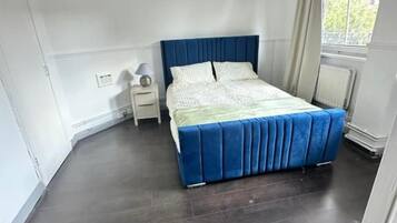 A bedroom with a bed, a nightstand, a window with curtains, and a radiator.