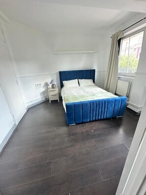 Un dormitorio con cama, mesita de noche, ventana con cortinas y radiador.