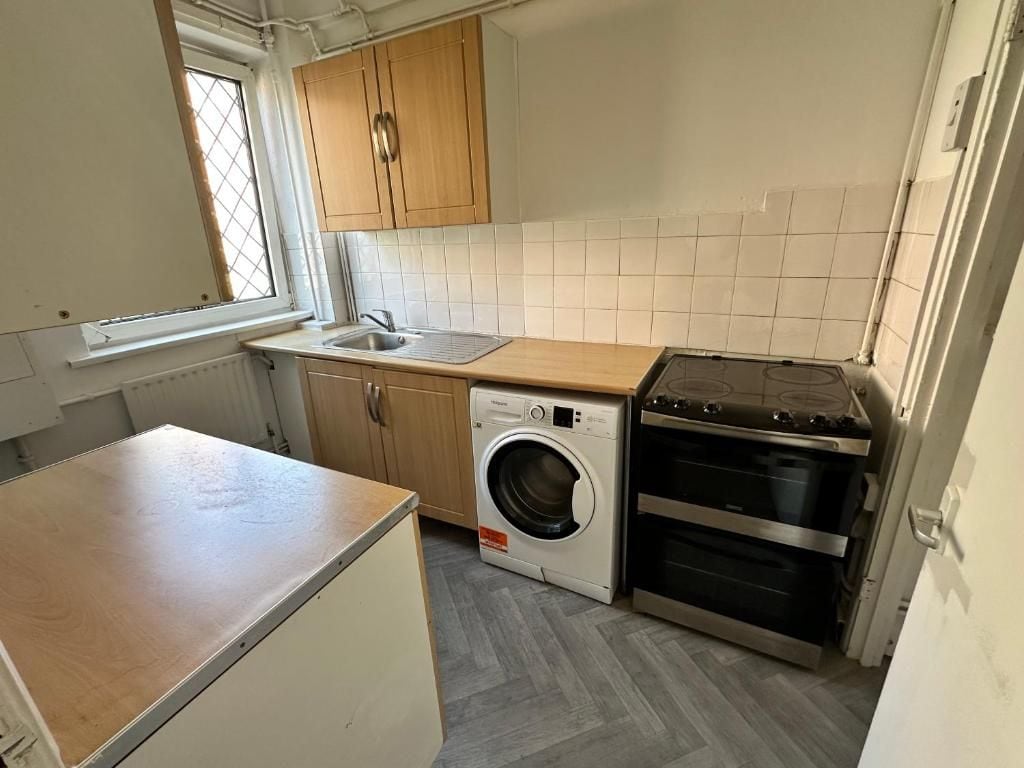 A compact kitchen with a washing machine, oven, and wooden cabinets.