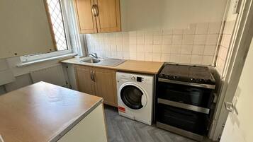 A compact kitchen with a washing machine, oven, and wooden cabinets.