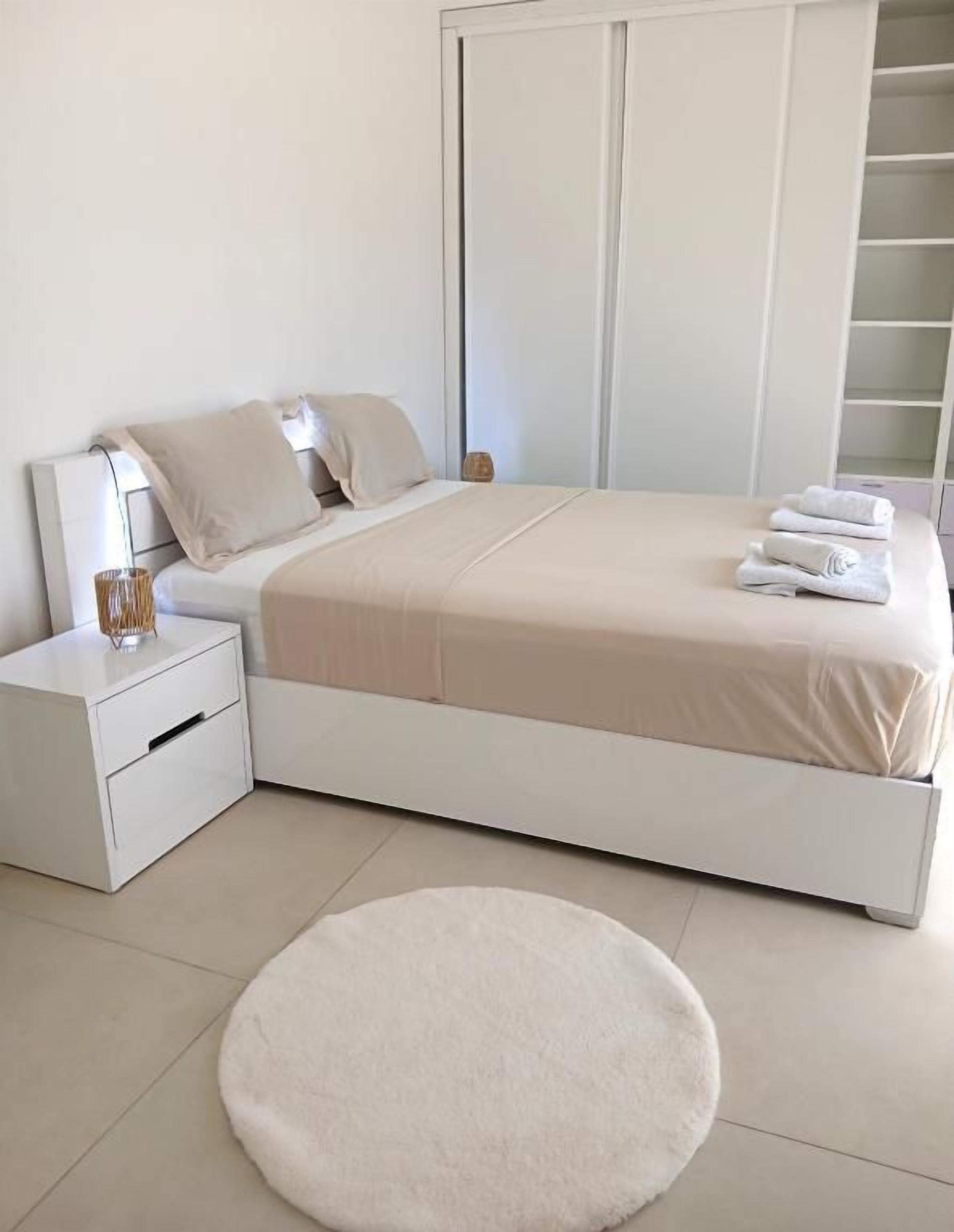 A bedroom with a bed, nightstand, and a round rug.