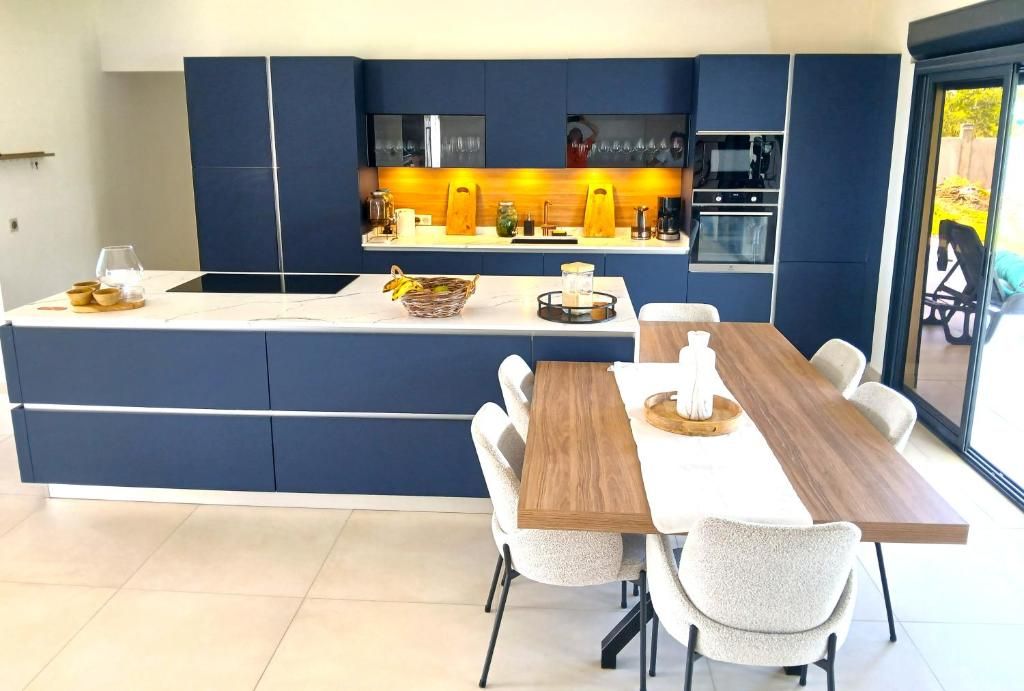 Une cuisine moderne dotée d’un îlot central, d’appareils électroménagers intégrés et d’un coin repas avec une longue table et des chaises en bois.