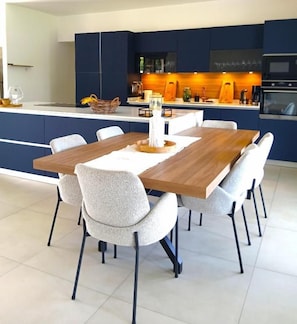 Una cocina moderna con armarios azul oscuro, una isla de madera y una zona de comedor con mesa y sillas de madera.