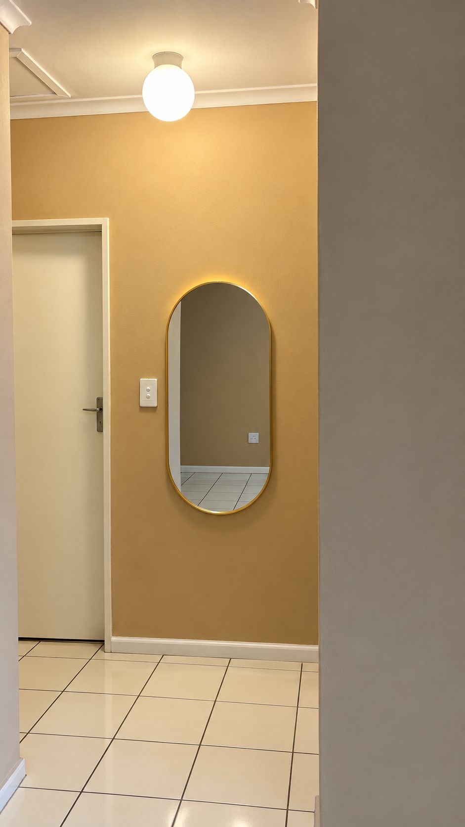 A hallway with a door, a wall-mounted mirror, and a ceiling light fixture.